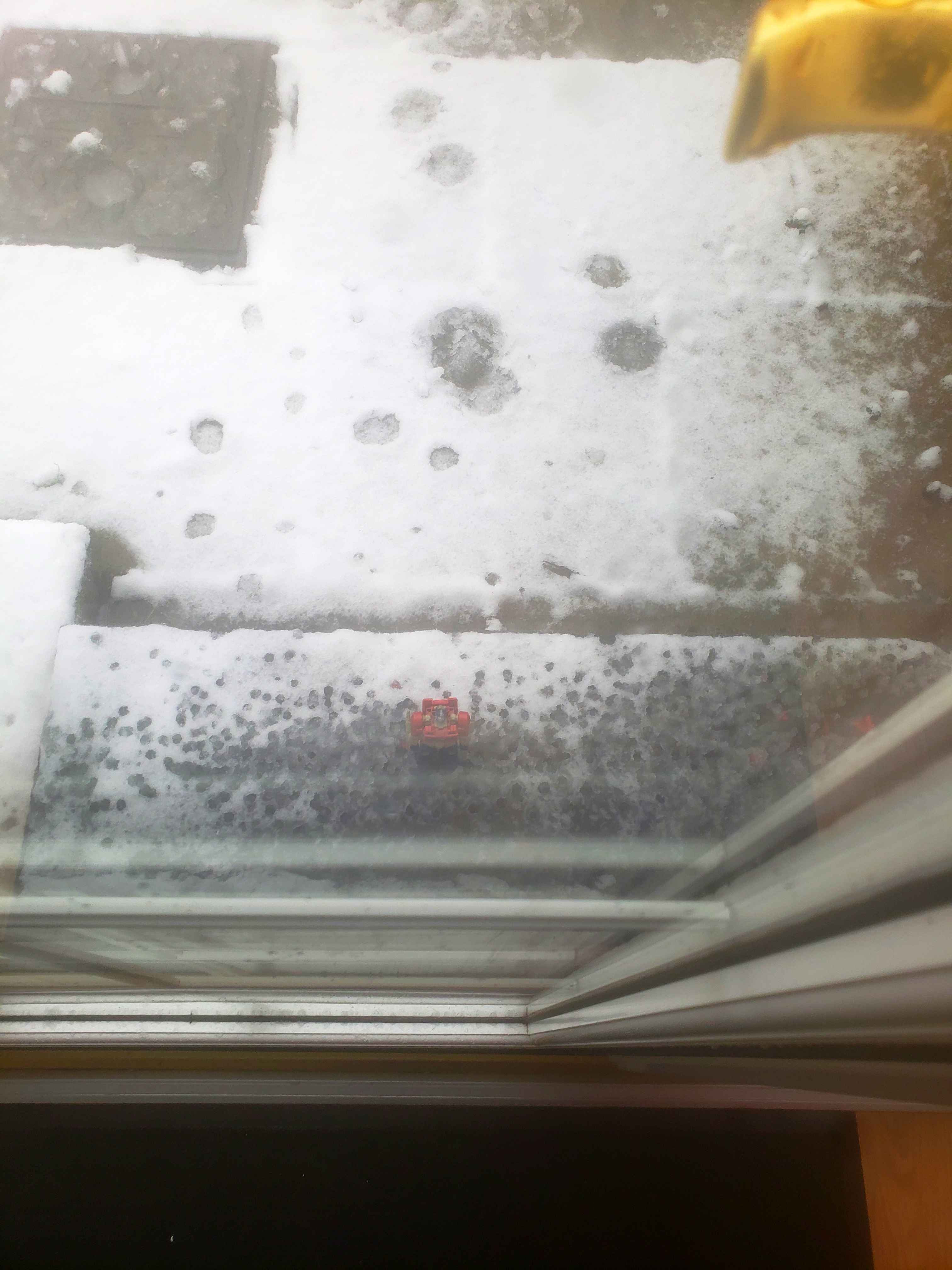 A photo of a glass door leading to a snowy yard. On the ground is a toy of Optimus Prime, who looks up pathetically at the viewer.