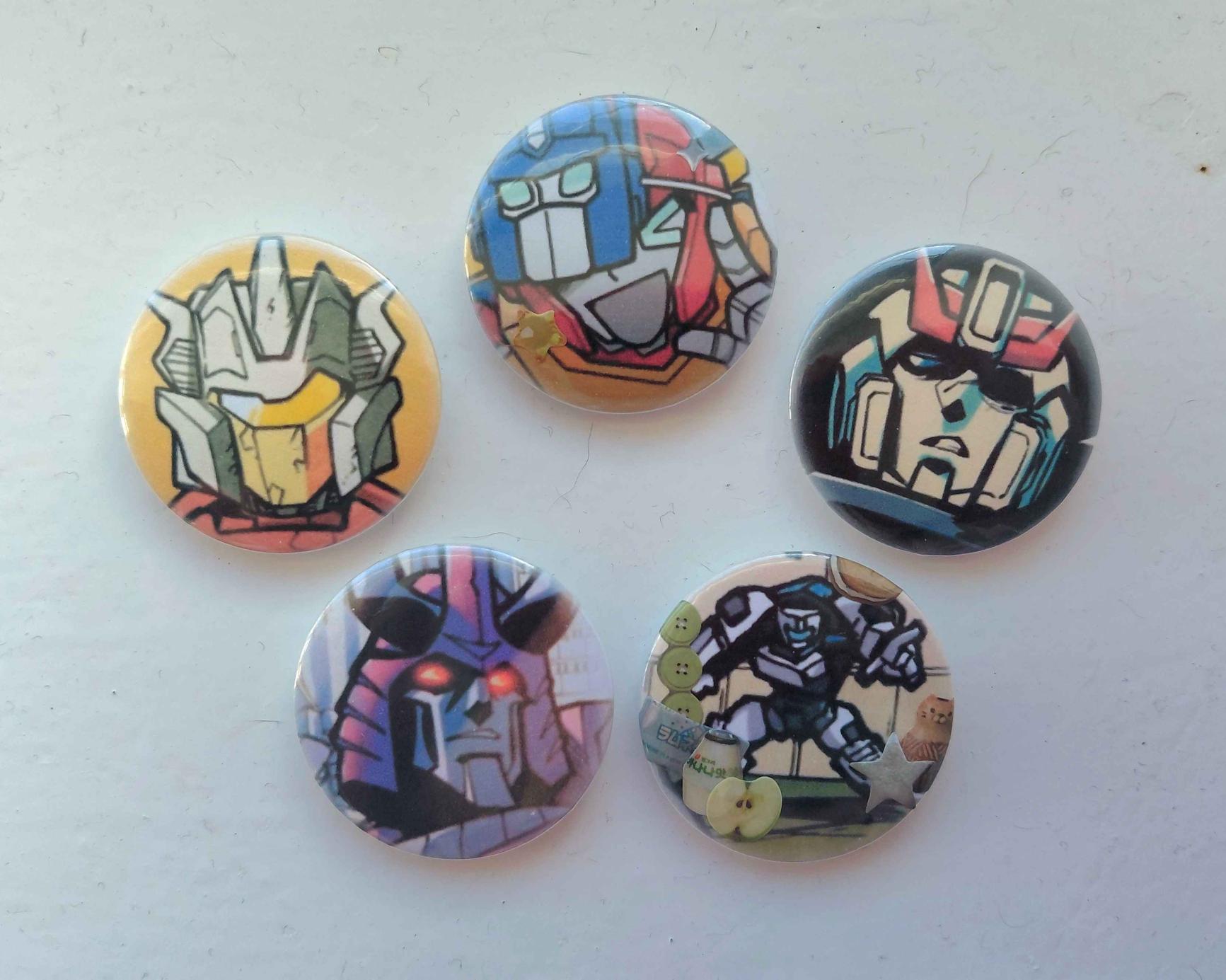 Five button pins. From left to right, they are of: IDW Chromedome; Tranformers Go! Go! Hot Rod; IDW Prowl; IDW Cyclonus; IDW Tailgate.